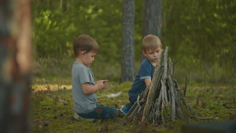 Two-boys-put-sticks-in-a-fire-in-the-woods-during-a-hike.-Boys-in-the-woods-prepare-to-light-a-fire-and-put-sticks-together